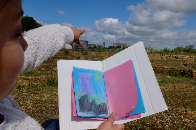 Child holding their drawing and pointing at distant building site